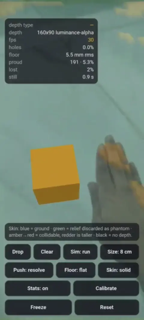 A virtual orange box on a desk shifting as a real hand moves past it, filmed through the phone in the WebXR depth demo